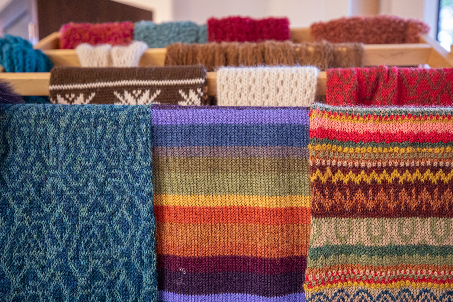 Halsdukar av ull i olika färger hänger på en ställning av trä.