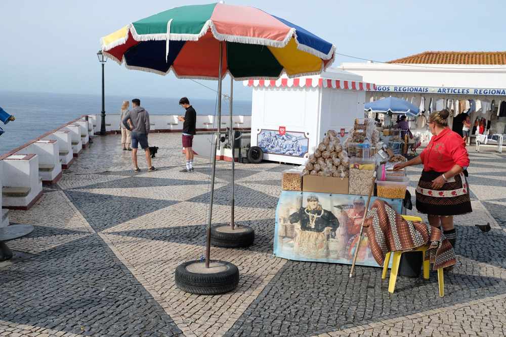 Olika stånd på ett torg vid havet. Kvinna i traditionella kläder.