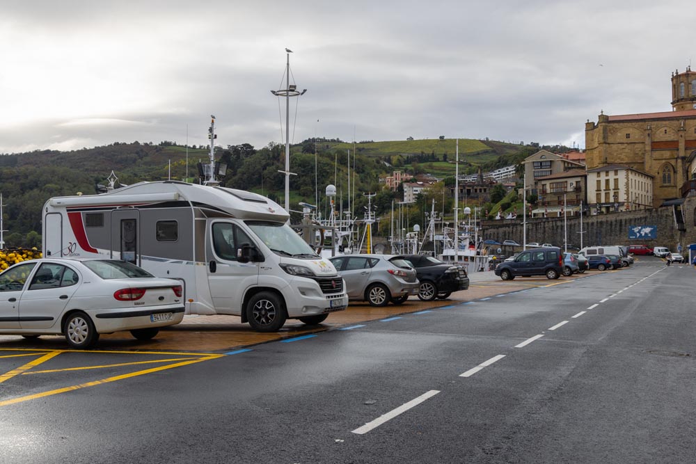 Parkering i hamnen i Getaria. En husbil och några andra bilar syns. I fjärran syns vackra gröna kullar.