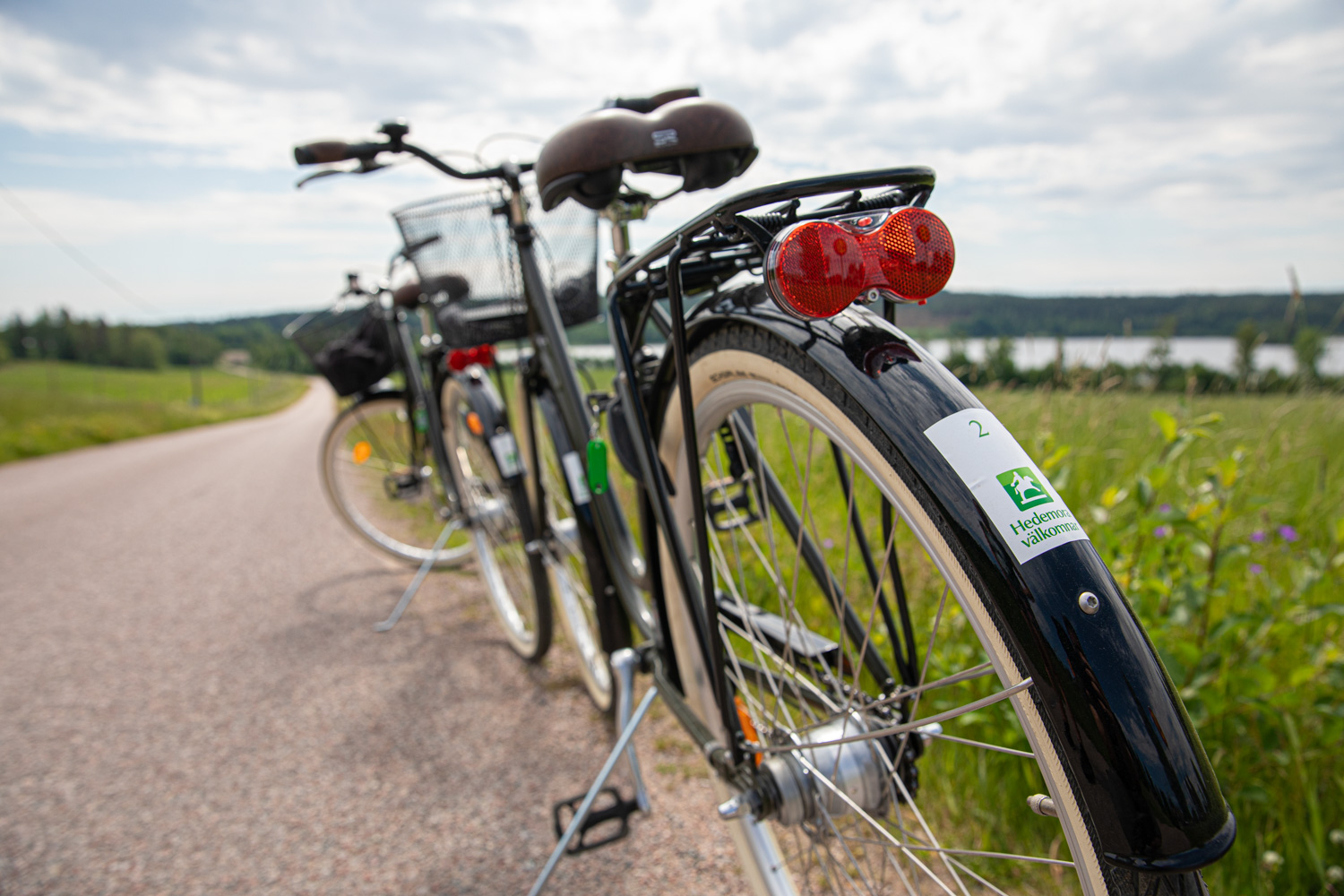 Två svarta hyrcyklar står efter en smal väg omgiven av ängar.