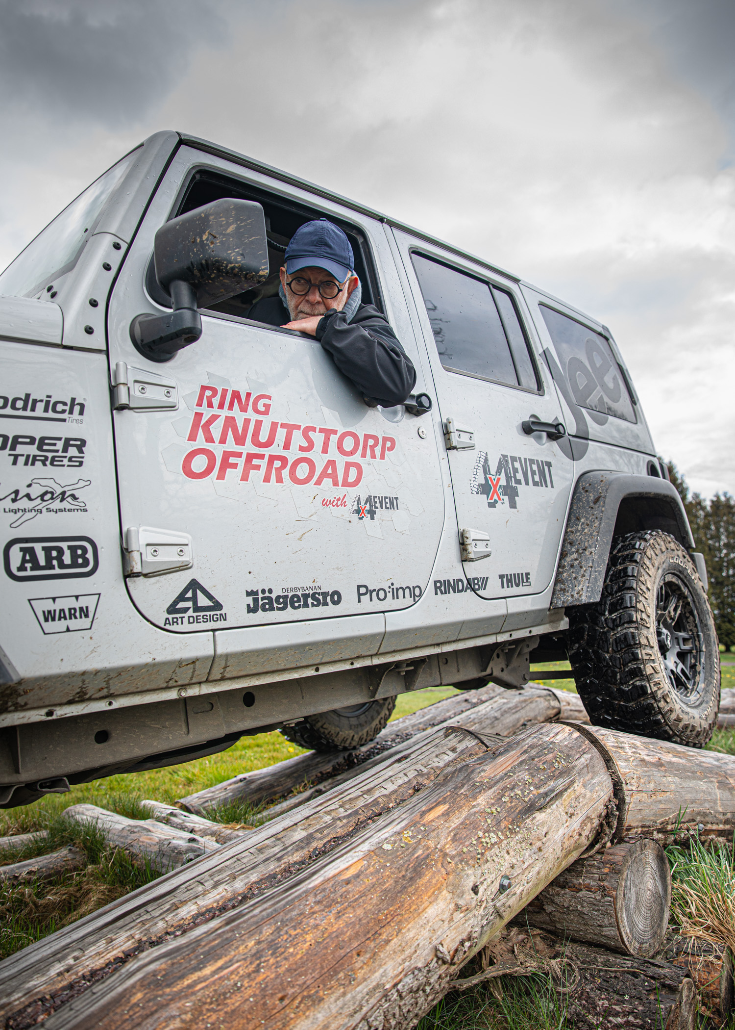 En man i en jeep uppepå några stockar.