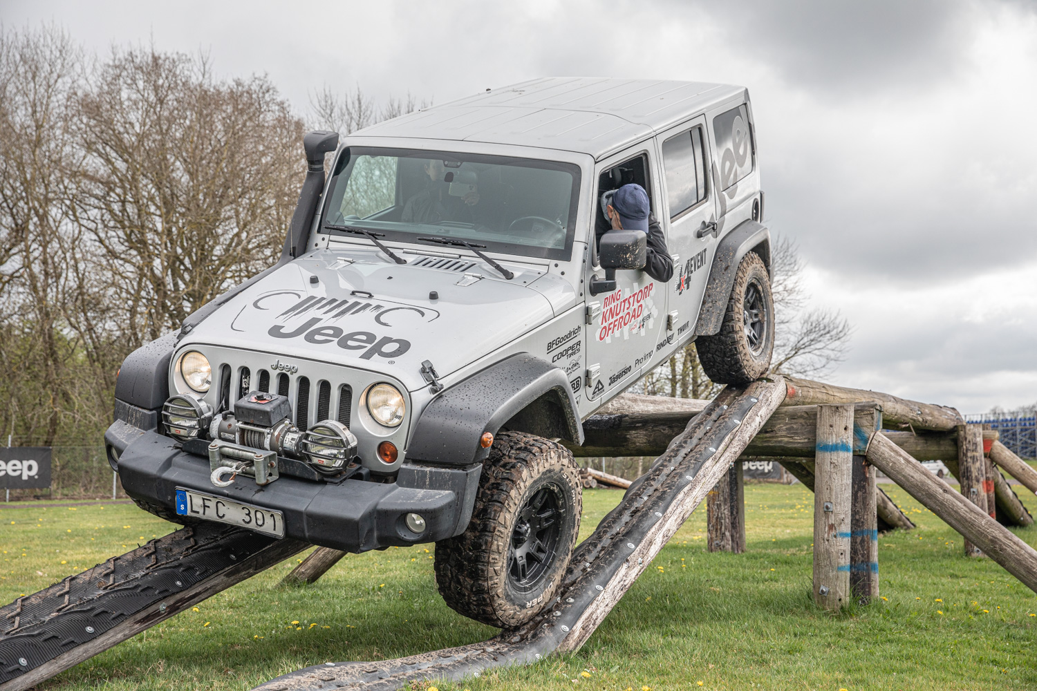 En Jeep på väg ner från ett hinder. Bilen lutar och balanserar på stockar med högerhjulen. Vänsterhjulen kör ner för en lite bredare spång.