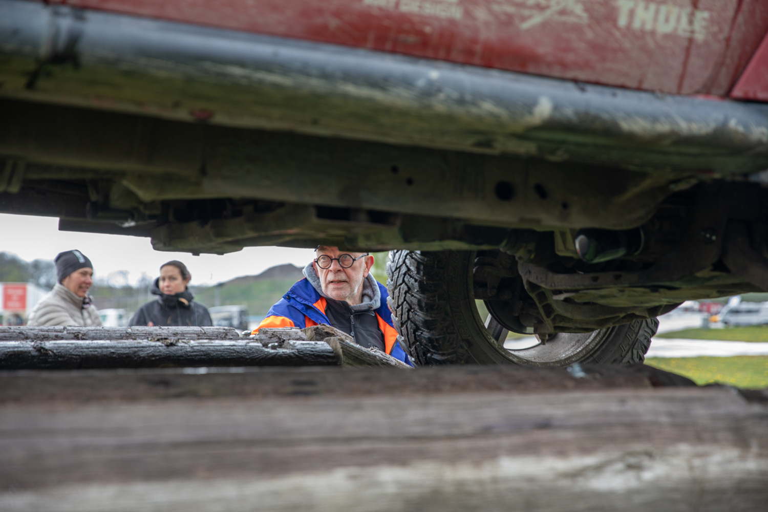 Underredet på en Jeep sedd från ögonhöjd. På andra sidan bilen syns tre personer.