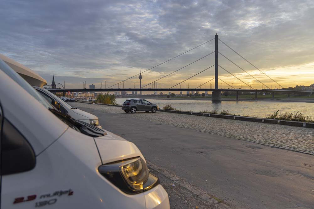 Fronten av en vit husbil syns på parkering vid floden Rhen.