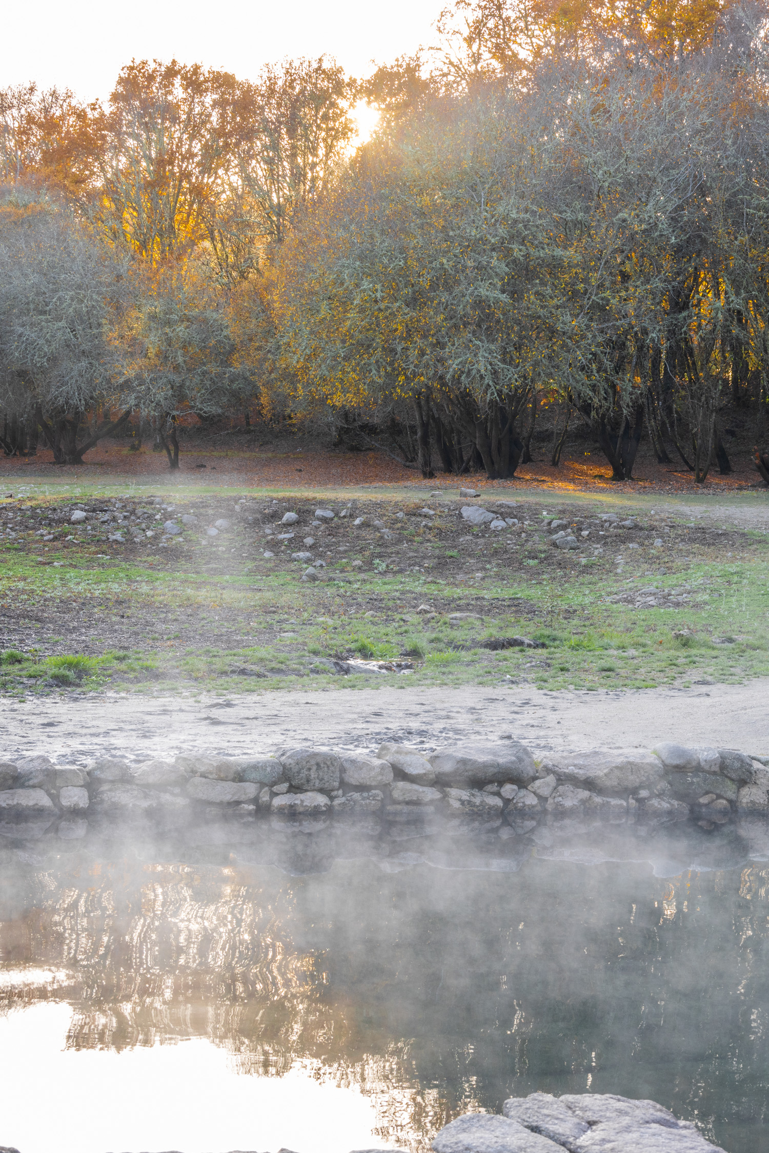 Det ryker från det varma vattnet i den varma källan omgärdad av sten.