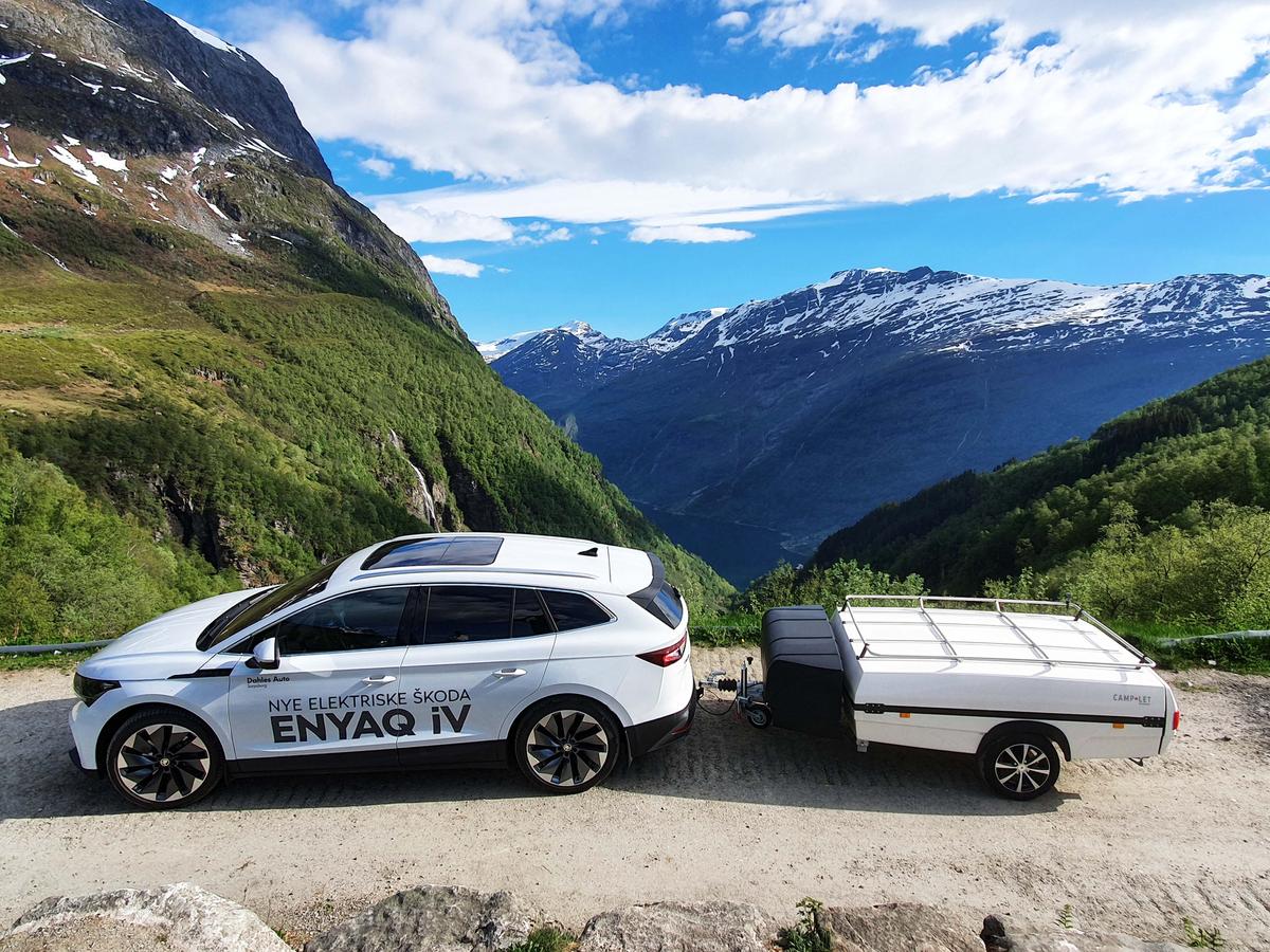 Vit el-bil av märket Skoda kör en vit Isabella camp-let på högt belägen grusväg med fjäll som utsikt.