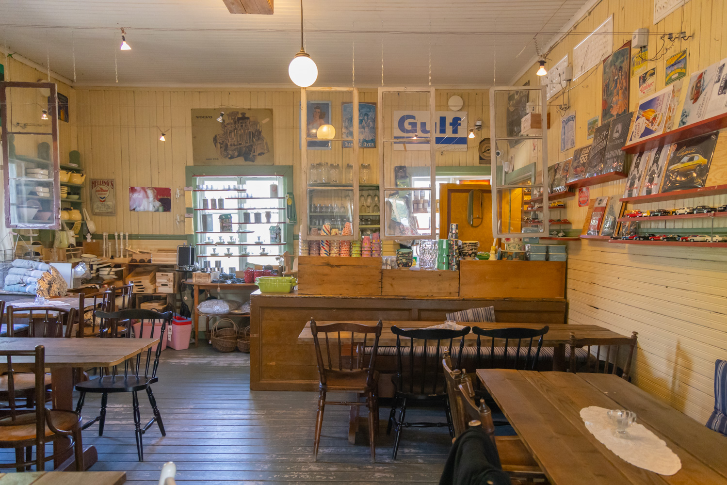 En vacker och gammaldags lokal med gula panelväggar, omaka trästolar och bord och en gammal köpmansdisk. Hyllor i olika färger på väggarna och gamla fönster hänger från taket vid disken.