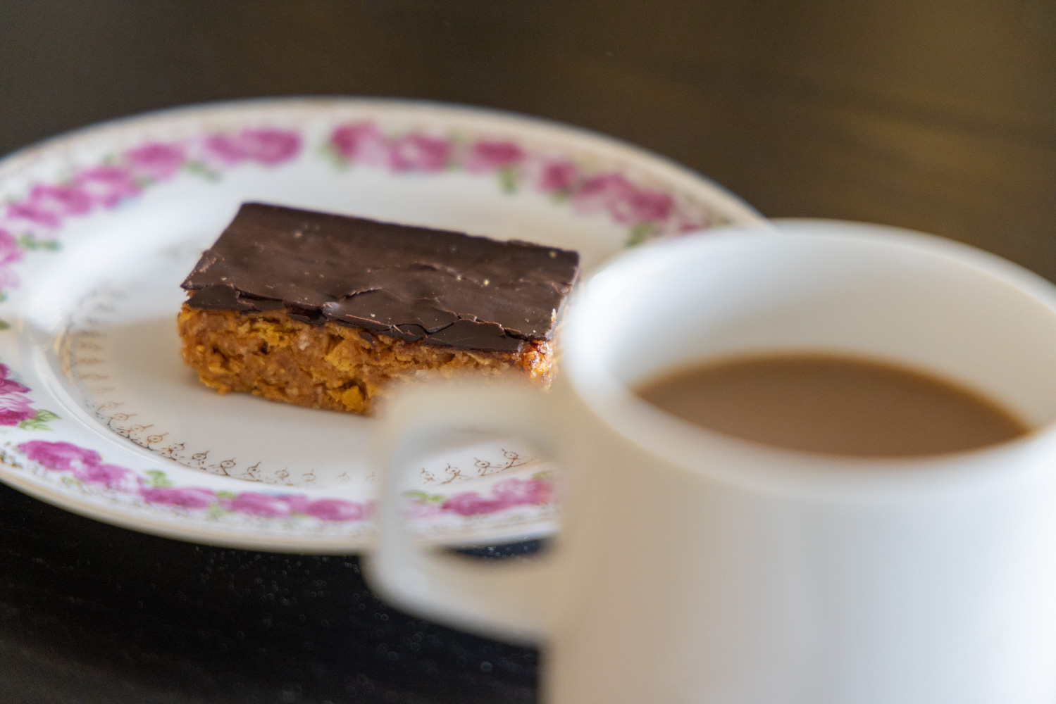 En kopp kaffe på ett bord. Bredvid finns en liten blommig assiett med Majas jordnötskaka.